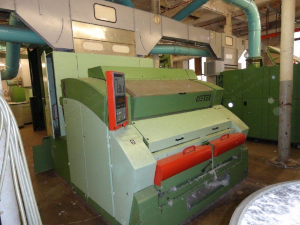A high production carding machine on a spinning mill floor, guards open, ducting overhead.