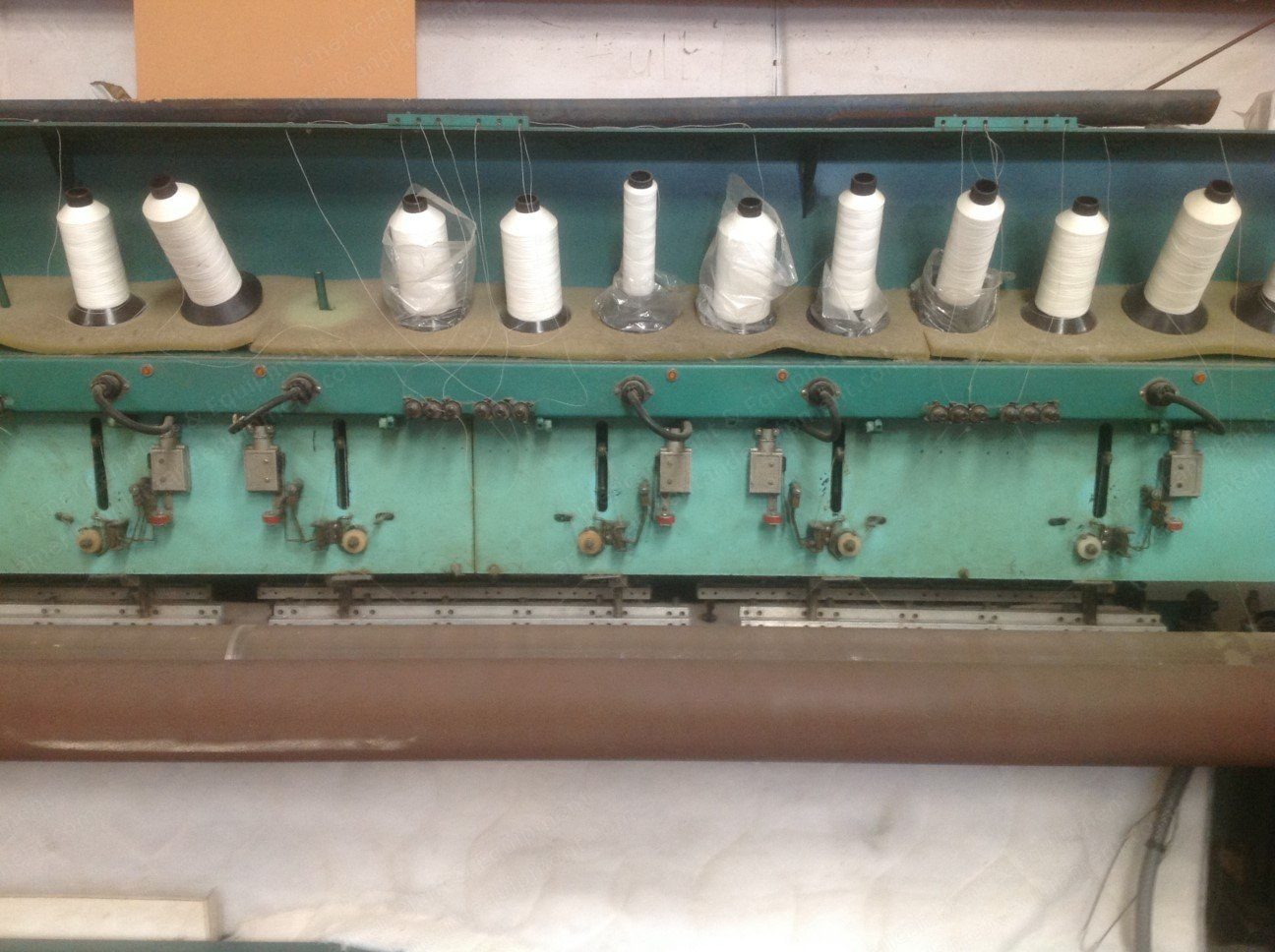 Row of thread spools on the creel of a mattress quilting machine.