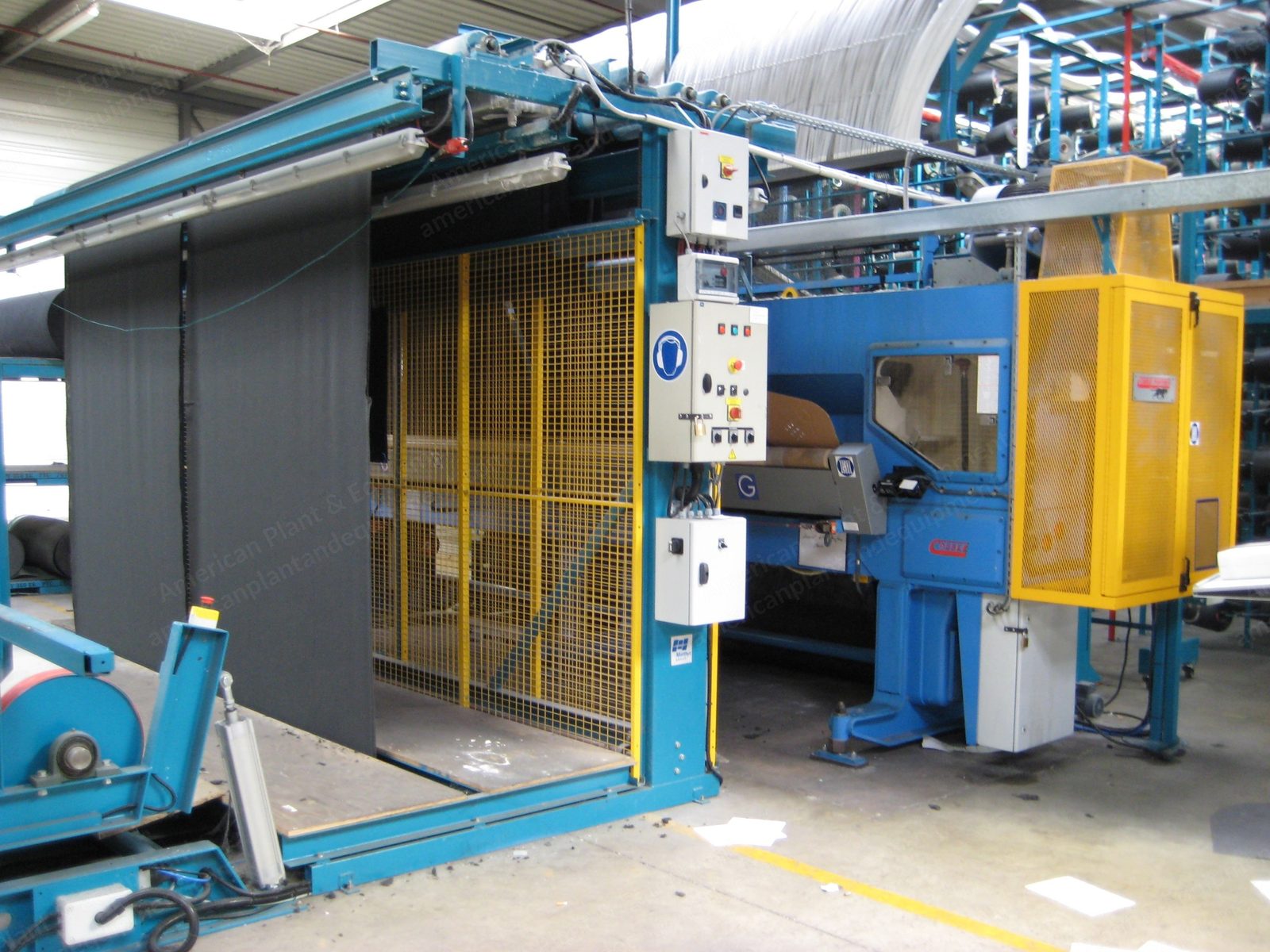 Wide tufting machine with blue guarding and a full-width creel behind it.