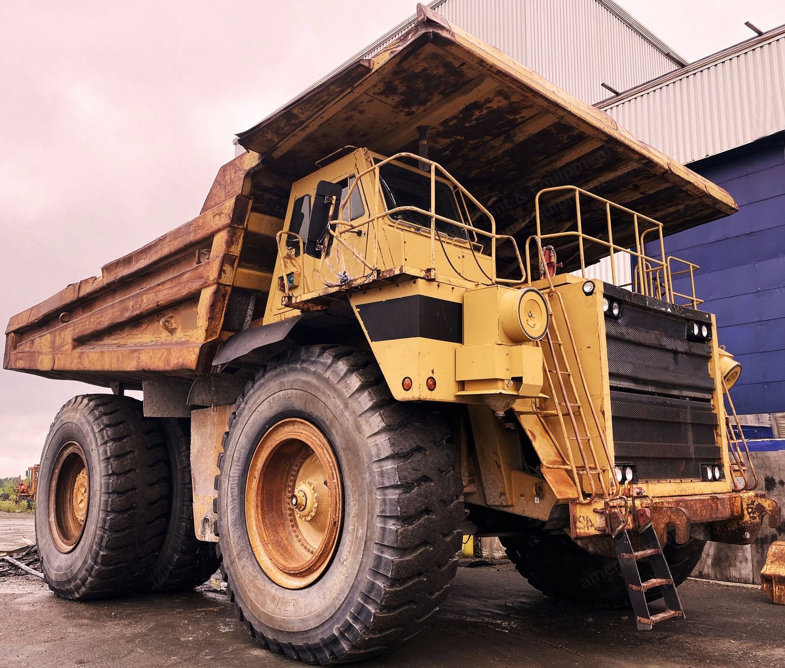 Rigid frame mining haul truck parked beside a workshop building.